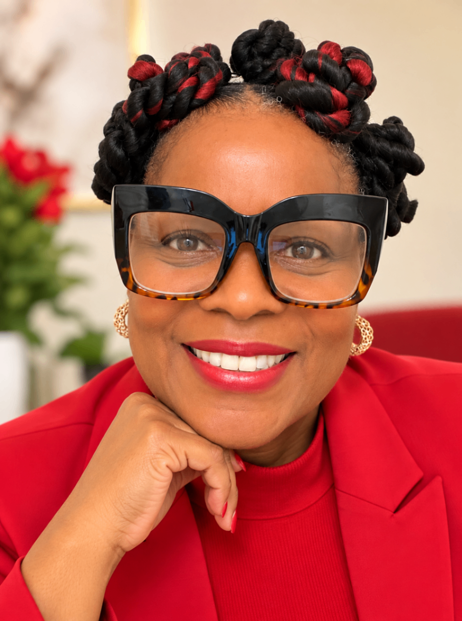 Portrait of Shirley Z. Jacobs wearing glasses and a red blazer, smiling, one hand raised to her chin.